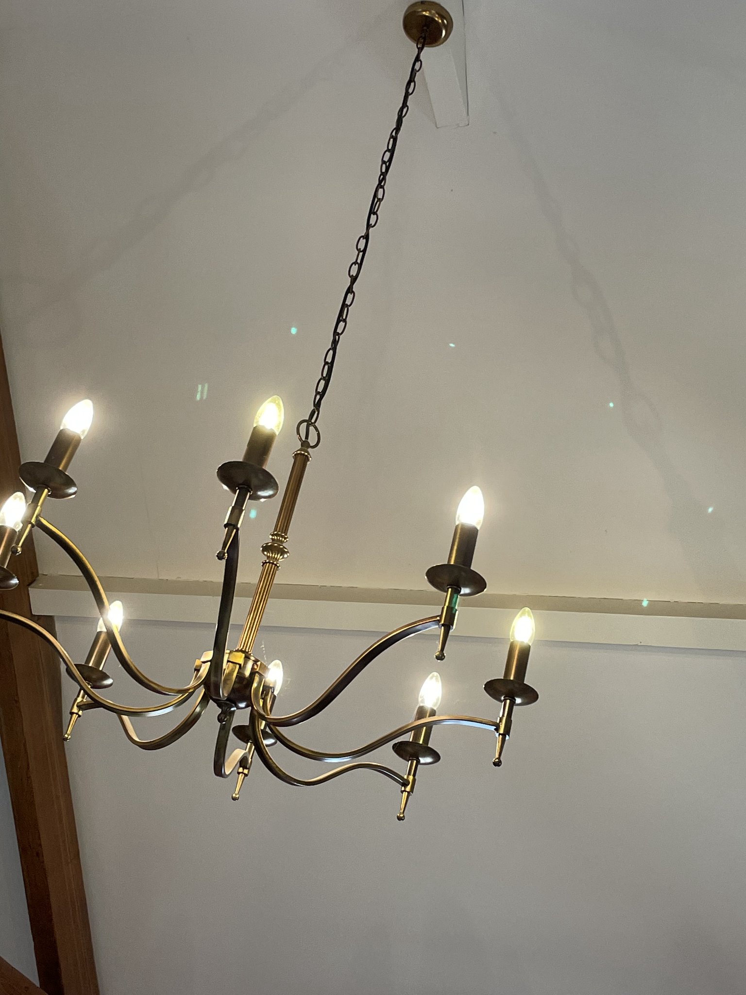 A brass candle-style chandelier fitted to a white ceiling