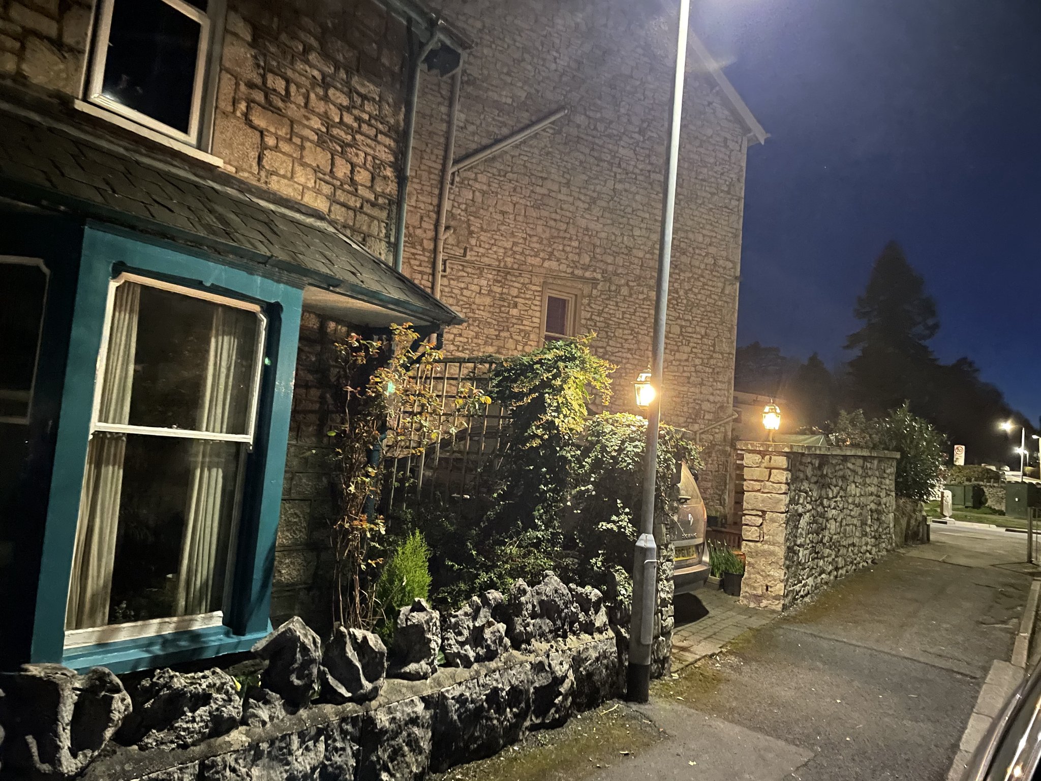 An outside light glowing at night beside the window of a stone cottage