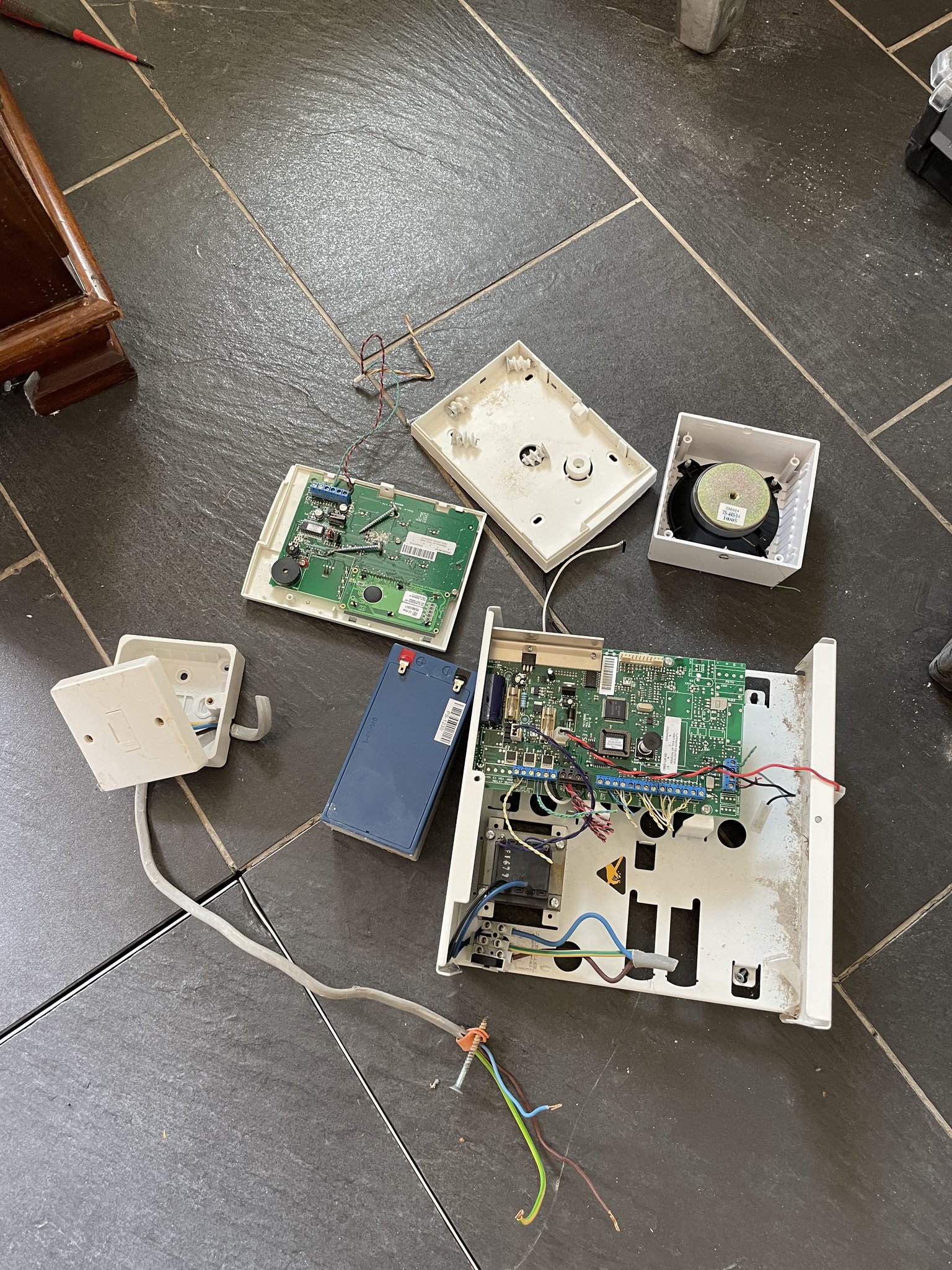 An old alarm control panel taken off the wall, lying on a slate floor
