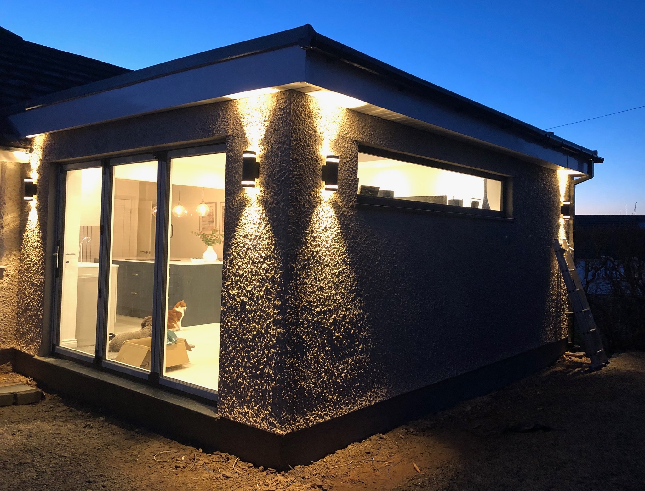 A finished house extension at dusk, its walls lit by new up and down wall lights