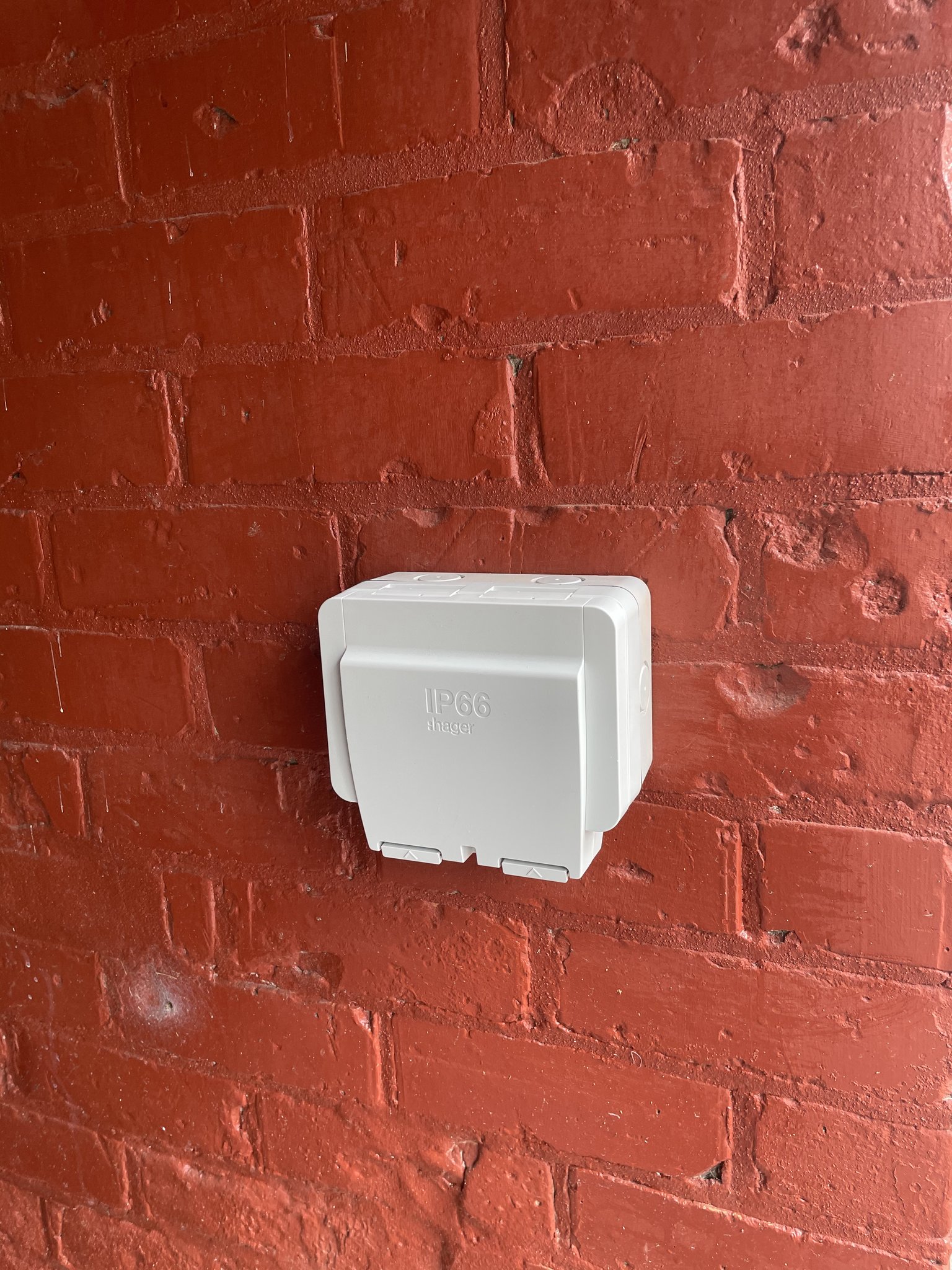 A weatherproof outdoor socket fitted on a red brick wall